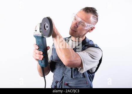 The builder in goggles, with an angle grinder in his hands. Stock Photo