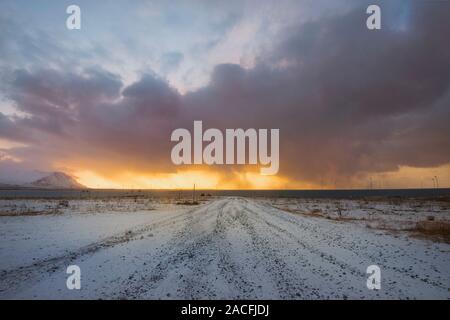 Looking down a road in Iceland, with a sunset sky on fire and storm clouds Stock Photo