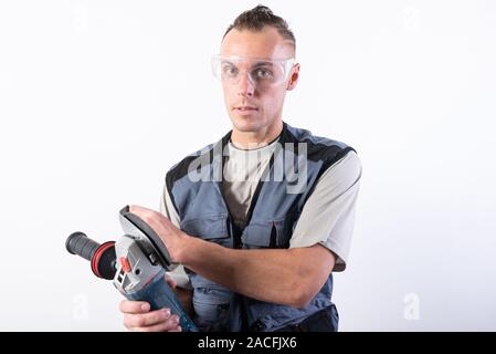 The builder in goggles, with an angle grinder in his hands. Stock Photo