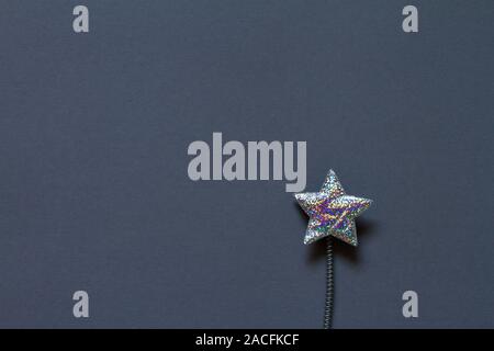 Close-up silver glitter plastic star with spring on gray background, minimalistic concept or background Stock Photo