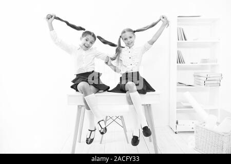 Successful team. Little schoolgirls classmates kids. Schoolgirls friends sit on desk. Best friends relaxing. Schoolgirls tidy hairstyle relaxing having rest. School uniform. Rebellious spirit. Stock Photo