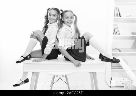 Schoolgirls friends sit on desk. Best friends relaxing. Schoolgirls tidy hairstyle relaxing having rest. School uniform. Rebellious spirit. School club. Little schoolgirls classmates friendly kids. Stock Photo