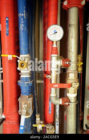 Insulated water pipes. This water supply is colour-coded: red for hot water and blue for cold. The dial is a pressure gauge. Stock Photo