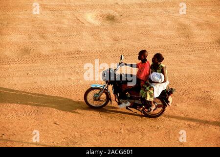 Riding a motorbike. Young man and a woman using a motorbike on an unpaved road. Photographed in Uganda. Stock Photo