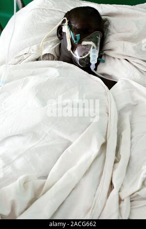 Hospital patient. The patient is sedated or sleeping, and is using an oxygen mask. Photographed at St. Mary's Hospital in Lacor, Gulu, Uganda. Stock Photo