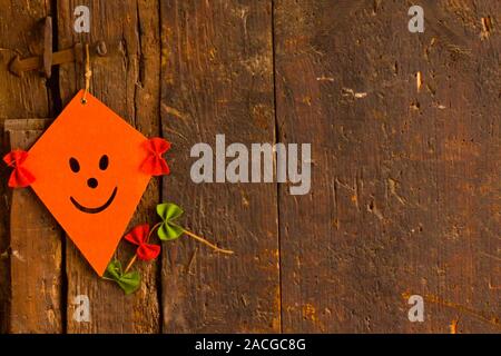 One colorful orange handmade felt kite with decorative multicolored bows on the tails mounted on an old wooden barn with copy space Stock Photo