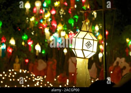 Traditional Thai paper lantern with monks in the blurred background and other colorful lanterns hanging on a tree captured at the Wat Phan Tao