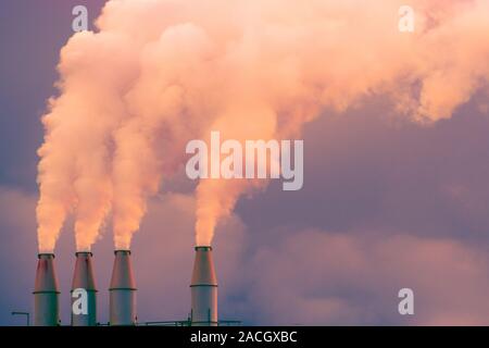 Smoke and steam rising into the air from power plant stacks; dark clouds background; concept for environmental pollution and climate change Stock Photo