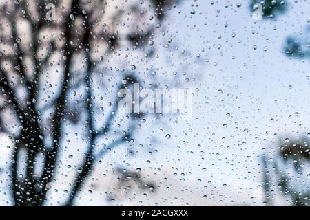 Drops of rain on the window; blue sky and blurred trees in the background Stock Photo