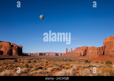 A hot air balloon flying in the Monument Valley Balloon Festival in the Monument Valley Navajo Tribal Park in Arizona.  The Three Sisters are at right Stock Photo