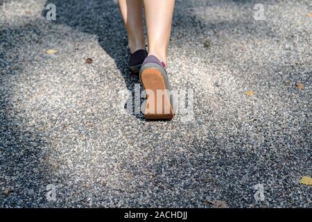 Female legs in sneakers are walking along the gravel path on a sunny summer day. Concept of an active lifestyle. Stock Photo