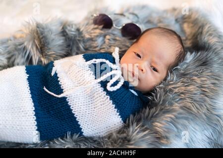 newborn baby boy swaddled in a knit wrap on a fur bed Stock Photo