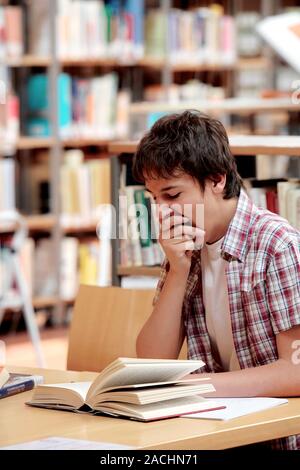 Library. Young man yawning whilst trying to study in a library. Stock Photo