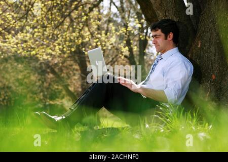 Office worker in a park using a laptop computer. Stock Photo