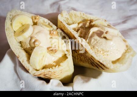 Pita pocket bread stuffed with caramel ice cream, walnuts and slices of banana, ready to eat, on old white cloth Stock Photo