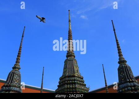 Beautiful stupa, or chedi in Thai language, of wat pho with blue sky background while a bird is flying past. Wat pho is a famous place in Bangkok Stock Photo