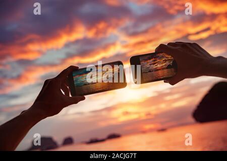 Two hands with mobile phones takes photo of beautiful sea bay sunset Stock Photo