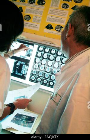 Brain CT scanning. Doctors assessing computed tomography (CT) scans of a patient's brain. CT scanning uses X-rays to obtain 2D and 3D images through b Stock Photo