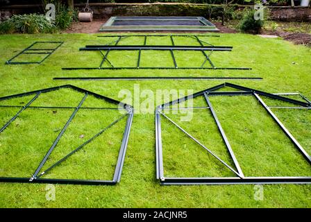 Domestic greenhouse under construction. The parts are laid out on a lawn in preparation for fitting to the base (in the background) which is anchored Stock Photo