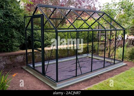 Domestic greenhouse under construction. The greenhouse structure is mounted on a base, complete with weed control fabric, but is unglazed. Stock Photo