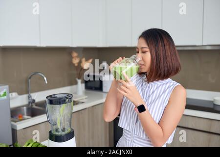 Asian woman drinking smoothie in the kitchen. Healthy concept. Stock Photo