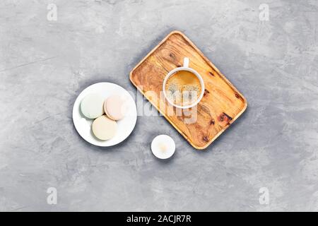 Gray concrete background with wooden tray and cup of espresso surrounded by marshmallows on a white plate. Flat lay, top view. Stock Photo