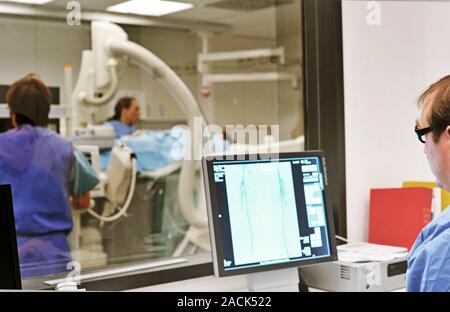 CT scan. Radiologist viewing the results of a computed tomography (CT) scan being carried out in the room beyond. CT is a diagnostic imaging technique Stock Photo