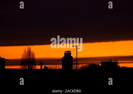 Wimbledon, London, UK. 3rd December 2019. A thin sliver of distant orange sunrise under an overhead blanket of cloud above suburban rooftops in south west London. Credit: Malcolm Park/Alamy Live News. Stock Photo