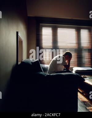 Depressed man sitting on a sofa in the living room of his house with his head in his hands. Stock Photo