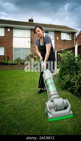 Dementia, conceptual image. Image of a woman vacuuming her lawn, representing the loss of cognitive ability associated with dementia. Stock Photo
