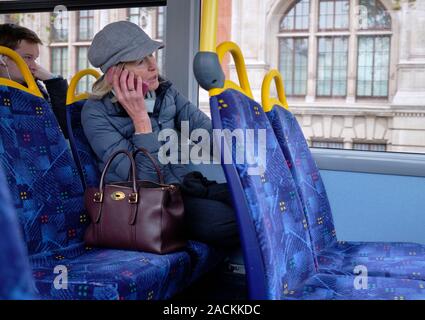 Woman sitting on blue seat on top level of double decker bus speaking on her mobile in London Stock Photo