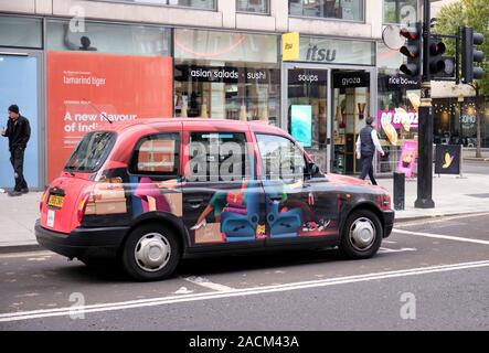 London black cab, with LouBoutin advertising, stopped at red light in front of Itsu restaurant. London, UK, November 19, 2019 Stock Photo