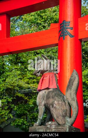 Kitsune (fox) statue wearing a red bib and holding a scroll in it's mouth, at the Fushimi Inari Shrine, Kyoto, Japan. Stock Photo