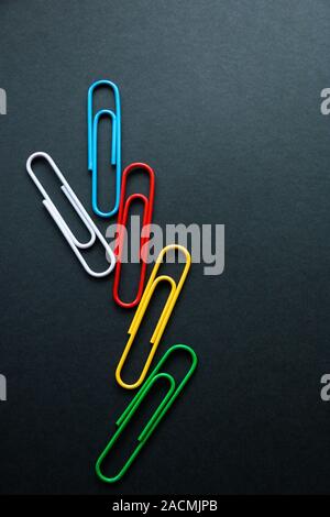 multi-colored paper clips on dark background, stationery. Stock Photo