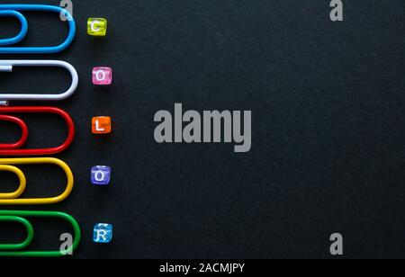 multi-colored paper clips and word color with small cubes on dark background, stationery. Stock Photo