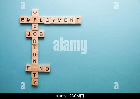 words related to work, to job search are collected in a crossword puzzle with wooden cubes on a blue background. Stock Photo