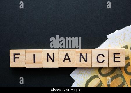 Finance words and money banknotes are collected in a crossword puzzle with wooden cubes on a dark background. Stock Photo
