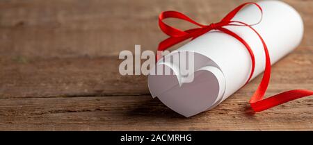 Love letter. Sheet of paper is twisted in the shape of a heart and tied to a bow. Wood background. Stock Photo