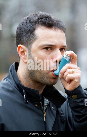 Asthma inhaler use. Man using an inhaler to treat an asthma attack. During an asthma attack, the small airways (bronchioles) in the lungs constrict, m Stock Photo