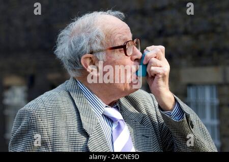 Asthma inhaler use. Elderly man using an inhaler to treat an asthma attack. During an asthma attack, small airways (bronchioles) in the lungs constric Stock Photo