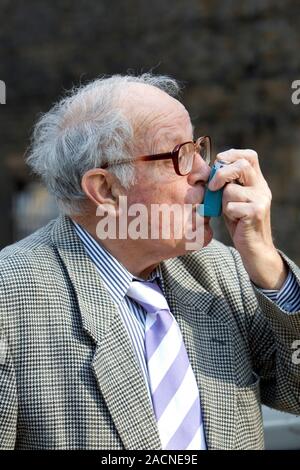 Asthma inhaler use. Elderly man using an inhaler to treat an asthma attack. During an asthma attack, small airways (bronchioles) in the lungs constric Stock Photo