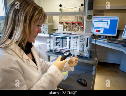 Electrochemical sensor production. Technician using a magnifying glass to examine a box of chemical sensors used in the manufacture of electrochemical Stock Photo