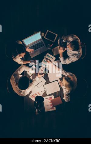 High angle above view vertical photo of four business partners sitting table working late night discussing new startup investment reading notebook Stock Photo