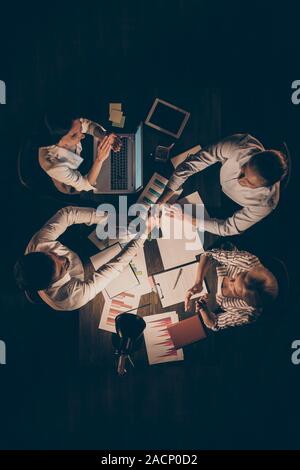 High angle above view vertical photo of four business partners sitting table working late night shaking hands signed contract ovation colleagues Stock Photo