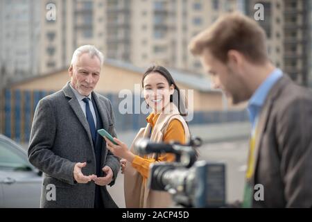 Young cute female reporter smiling to a videocamera Stock Photo
