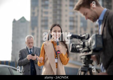 Young cute female reporter talking to a videocamera Stock Photo