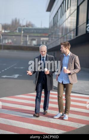 Young businessman and his marure mentor crossing the street having a break at work Stock Photo