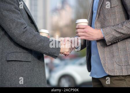 Two men with coffee cups shaking each others hand Stock Photo