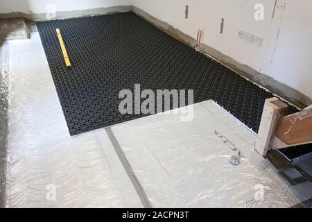 Laying underfloor heating. Matting (black) being laid on the floor of a home to hold an underfloor heating system. The system consists of cabling that Stock Photo