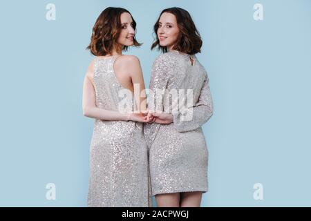 Two twin sisters in shiny evening dresses, holding hands Stock Photo